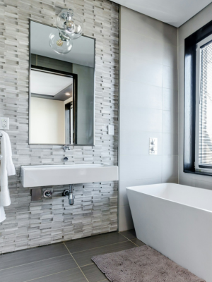 A remodeled bathroom with grey tile and white tub.