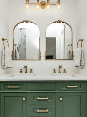 A modern bathroom with double vanity, green cabinets and gold overhead lighting.